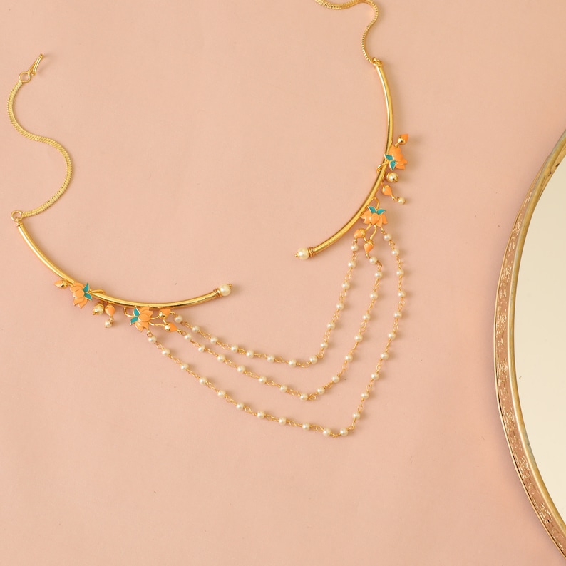 May include: A gold nose ring with a curved bar and a dangling chain of pearls. The chain has three strands and is decorated with small orange and green flowers.