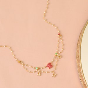May include: A delicate gold chain necklace with white pearls and pink and green enamel flower accents.