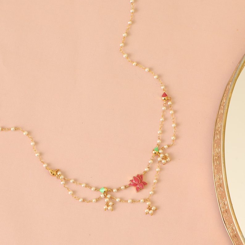May include: A delicate gold chain necklace with white pearls and pink and green enamel flower accents.