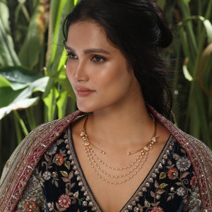 May include: A woman wearing a gold choker necklace with a floral design and a multi-strand pearl necklace. She is wearing a dark blue embroidered dress with a red and gold shawl.