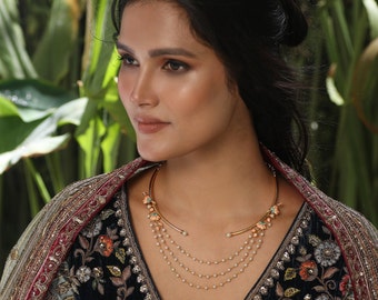 May include: A woman wearing a gold choker necklace with a floral design and a multi-strand pearl necklace. She is wearing a dark blue embroidered dress with a red and gold shawl.