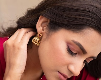 May include: Gold earrings with a red stone in the center. The earrings are small and have a traditional Indian design.