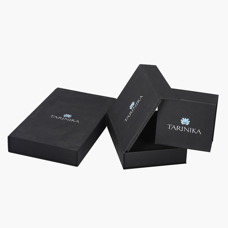 May include: Three black gift boxes with the logo "TARINIKA" printed on each. The logo features a stylized blue flower.