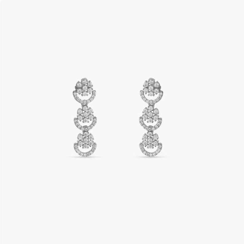 May include: A pair of silver dangle earrings with three tiers of round, sparkly, white stones.