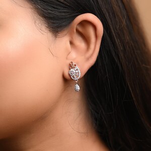 May include: A pair of silver earrings with a teardrop-shaped pendant and a cluster of small, clear stones.
