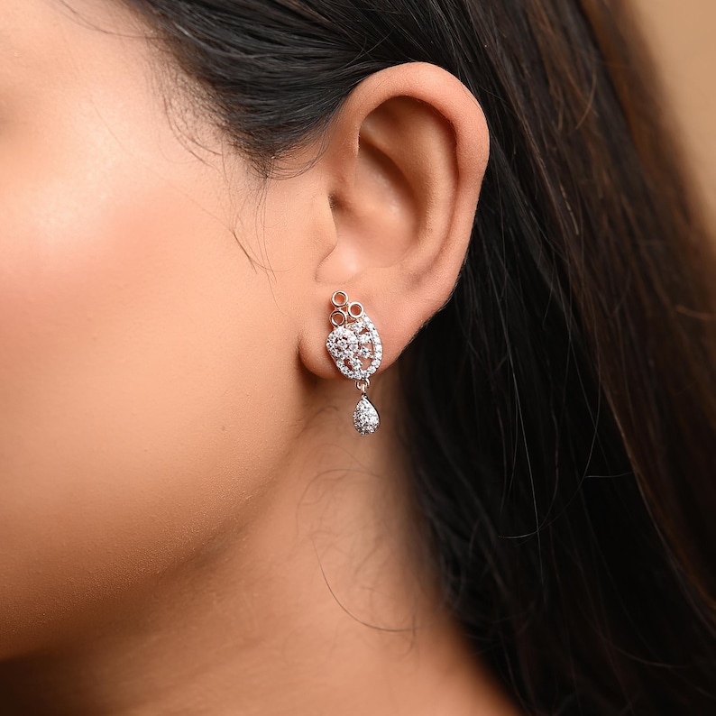 May include: A pair of silver earrings with a teardrop-shaped pendant and a cluster of small, clear stones.