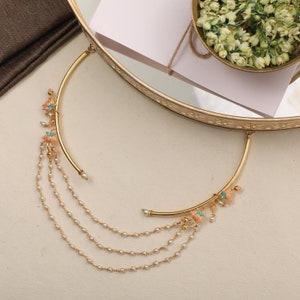 May include: A gold necklace with a delicate chain and a pendant featuring a cluster of pink and turquoise flowers. The pendant is attached to a curved bar.