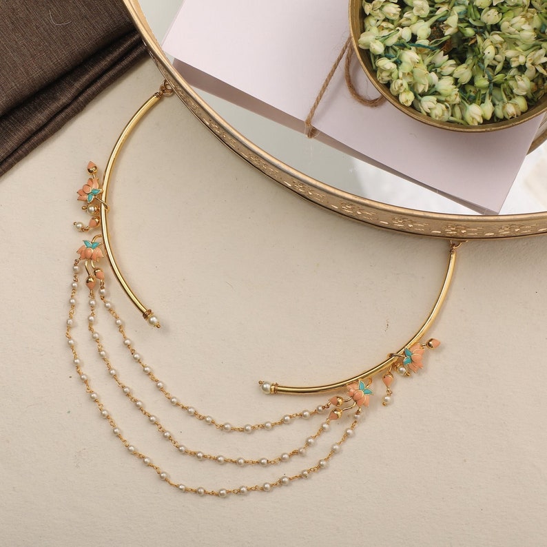 May include: A gold necklace with a delicate chain and a pendant featuring a cluster of pink and turquoise flowers. The pendant is attached to a curved bar.