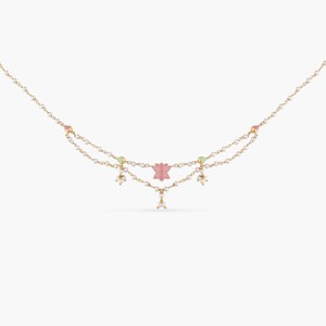 May include: A delicate gold necklace with a pink lotus flower charm and white pearl accents. The necklace has two strands of pearls and is perfect for adding a touch of elegance to any outfit.