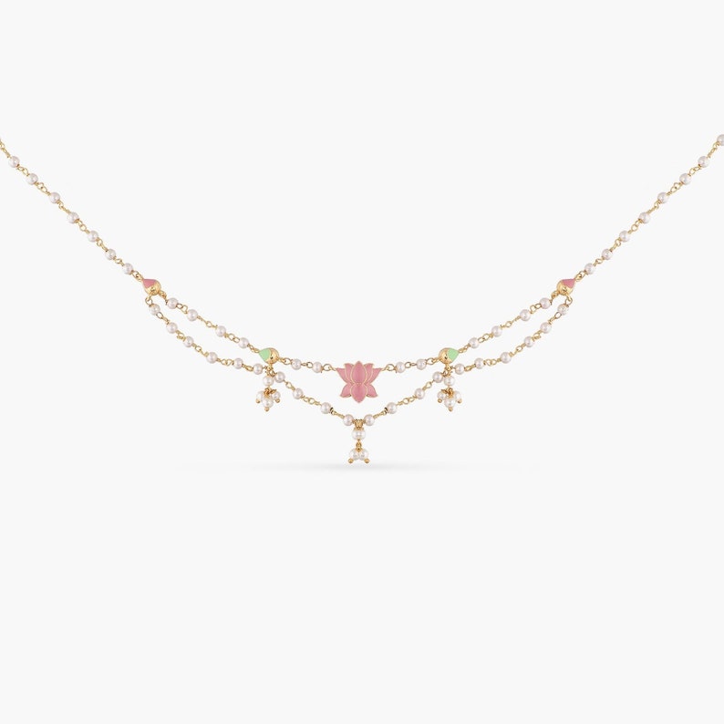 May include: A delicate gold necklace with a pink lotus flower charm and white pearl accents. The necklace has two strands of pearls and is perfect for adding a touch of elegance to any outfit.