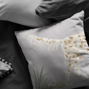 May include: A white throw pillow with a brown and white spotted dog design. The dog is lying down with its tail curled up. The pillow is on a gray bed with other pillows.