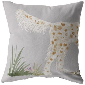 May include: A gray throw pillow with a white and brown spotted dog illustration. The dog is facing away from the viewer and has its tail raised. The background is a light gray with green grass and pink flowers.