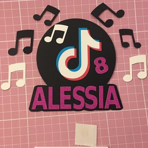 May include: A black and white TikTok logo with a red and blue accent on a black circle with musical notes around it. The text "Alesssia" is in pink glitter below the logo and the number "8" is in pink glitter to the right of the logo.