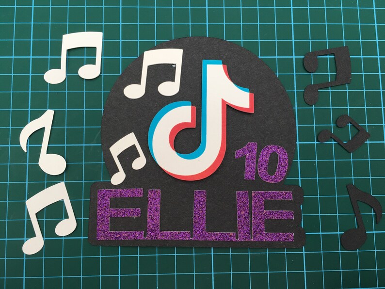 May include: A black and white TikTok logo with a red and blue outline, surrounded by white musical notes. The name "ELLIE" is written in purple glitter letters with the number "10" in purple glitter next to it.