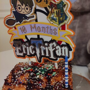 May include: A chocolate cake with sprinkles and a Harry Potter themed cake topper. The topper features a character from the Harry Potter series, the number 9 3/4, and the Hogwarts crest. The cake topper also includes the text "10 Months Eric Trifan".