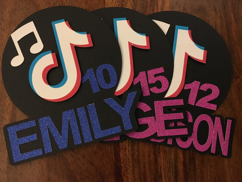 May include: Three black and white TikTok logo party decorations with glitter text. The text reads "Emily 10", "Age 15", and "12 years old".