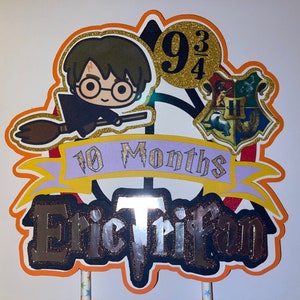 May include: A Harry Potter themed cake topper with a cartoon image of Harry Potter on a broomstick, a Hogwarts house crest, and the text "10 Months Eric Trifan 9 3/4".