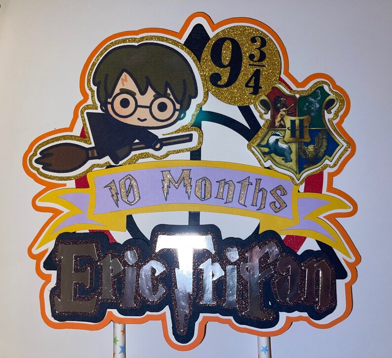 May include: A Harry Potter themed cake topper with a cartoon image of Harry Potter on a broomstick, a Hogwarts house crest, and the text "10 Months Eric Trifan 9 3/4".
