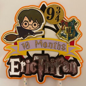 May include: A Harry Potter themed cake topper with a cartoon character holding a broom, a Hogwarts house crest, and the text "9 3/4", "10 Months", and "Eric Trifan".