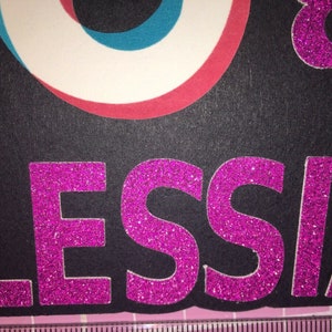 May include: A black background with the name "ALESSIA" in pink glitter letters.