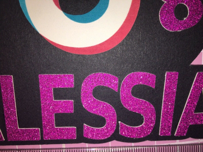May include: A black background with the name "ALESSIA" in pink glitter letters.