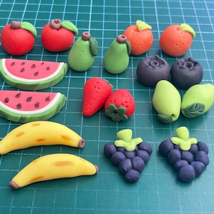 May include: A collection of colourful, handmade fruit and vegetable charms, including watermelon, bananas, grapes, strawberries, pears, oranges, and limes. These miniature food charms are perfect for adding a touch of whimsy to jewellery, keychains, or other crafts.