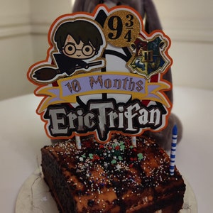 May include: A chocolate cake with sprinkles and a Harry Potter themed topper. The topper features a cartoon of Harry Potter on a broomstick, a Hogwarts house crest, and the text "10 Months Eric Trifan".