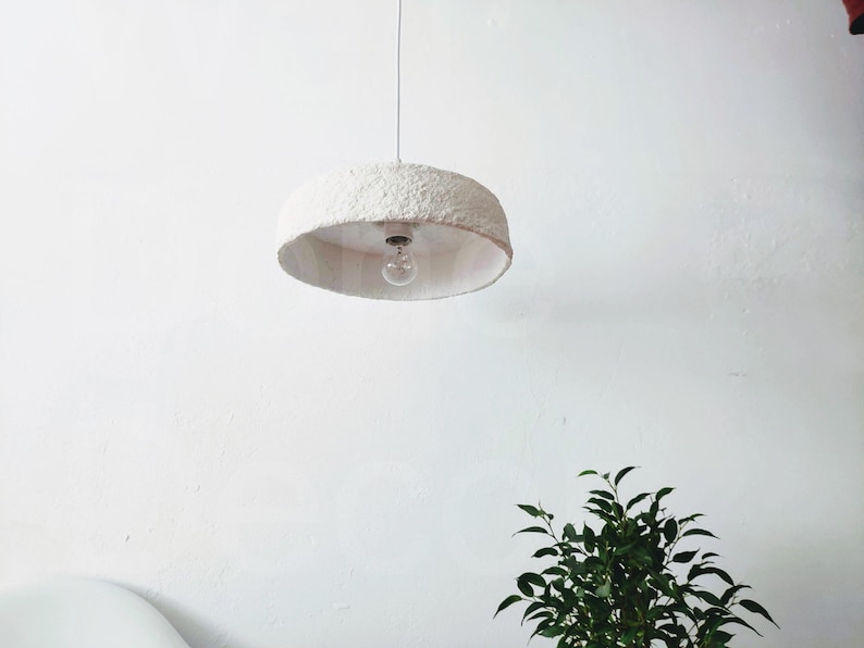 May include: A white, round, textured pendant light fixture with a single light bulb hanging from a white ceiling.
