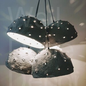 May include: A set of four gray paper pendant lights with a textured surface and small holes throughout. The lights are hanging from the ceiling and are illuminated.