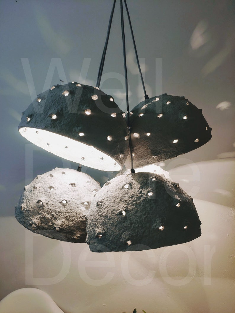 May include: A set of four gray paper pendant lights with a textured surface and small holes throughout. The lights are hanging from the ceiling and are illuminated.