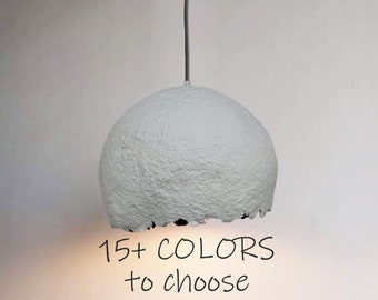 May include: A white paper pendant light with a textured surface. The light is hanging from a gray cord. The text "15+ COLORS to choose" is written below the light.