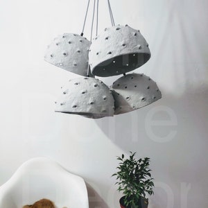 May include: A set of five gray paper pendant lights with holes throughout the surface. The lights are hanging from a white ceiling.