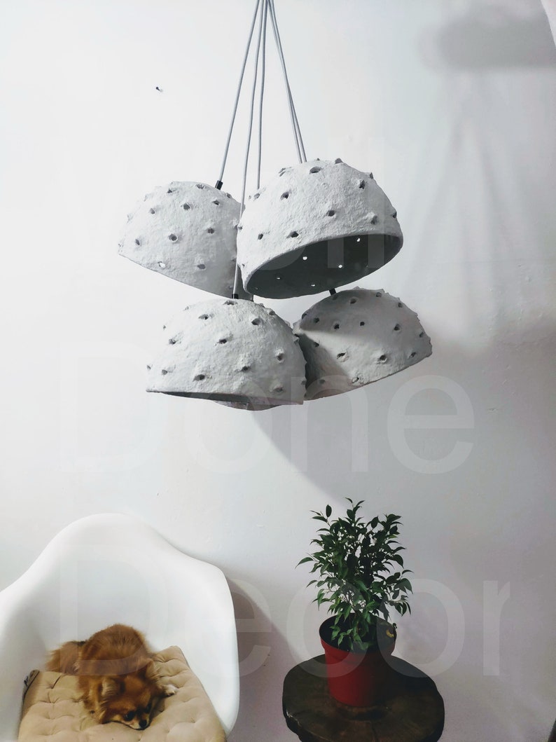 May include: A set of five gray paper pendant lights with holes throughout the surface. The lights are hanging from a white ceiling.