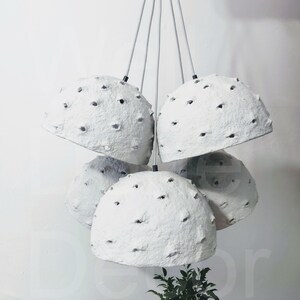 May include: A set of five white paper pendant lights with a textured surface and small holes throughout. The lights are hanging from black cords.