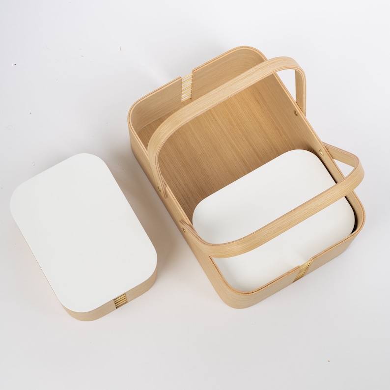 May include: A wooden basket with a white liner and a handle. The basket is made of natural wood and has a woven design. The liner is made of a smooth, white material.
