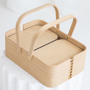 May include: A wooden basket with two compartments and two handles. The basket is made of light wood and has a natural finish.