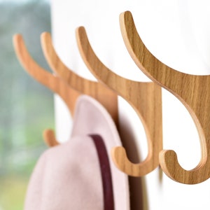 May include: A wooden wall-mounted coat rack with four hooks. The hooks are shaped like a stylized branch with a curved design. A hat is hanging on one of the hooks.