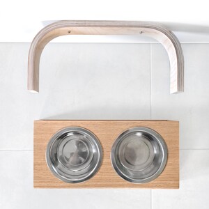 May include: A wooden pet food stand with two stainless steel bowls. The stand has a curved wooden bar that can be mounted to a wall.