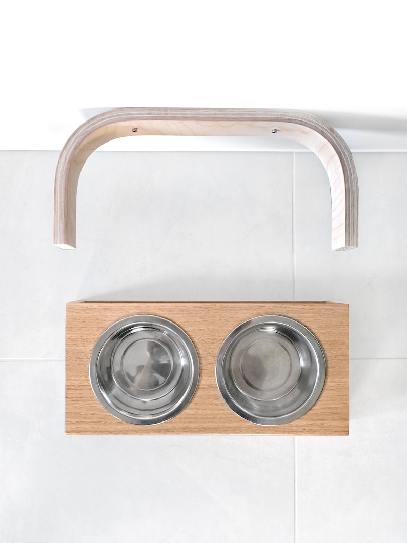 May include: A wooden pet food stand with two stainless steel bowls. The stand has a curved wooden bar that can be mounted to a wall.