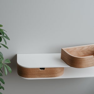 May include: A white wall-mounted shelf with two curved compartments. The top compartment is made of light wood and the bottom compartment is made of white wood with a light wood trim.