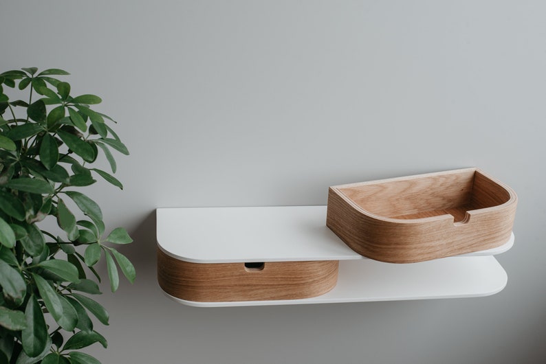 May include: A white wall-mounted shelf with two curved compartments. The top compartment is made of light wood and the bottom compartment is made of white wood with a light wood trim.