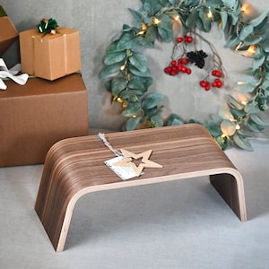 May include: A wooden step stool with a curved design. The stool is made of walnut wood and has a natural finish. A small wooden star is on top of the stool.
