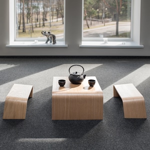May include: A wooden table with a black teapot and two cups, set on a gray carpet. Two wooden benches are on either side of the table.