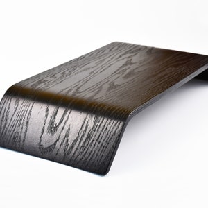 Peut inclure: Un support pour ordinateur portable en bois noir avec un design incurvé. Le support est en bois avec un motif de grain naturel.