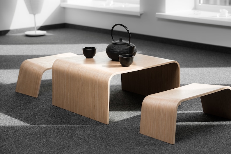 May include: A wooden coffee table with a curved edge and two matching wooden stools. A black teapot and three black teacups are on the table.