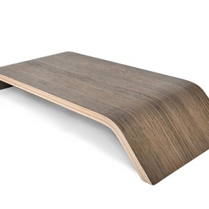 May include: A wooden laptop stand with a curved design. The stand is made of light brown wood with a darker brown stain. It is designed to elevate a laptop to a more ergonomic height.
