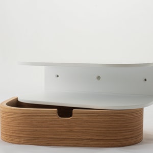 May include: White wall-mounted shelf with a curved front and a wooden drawer underneath. The shelf has three screw holes on the back.