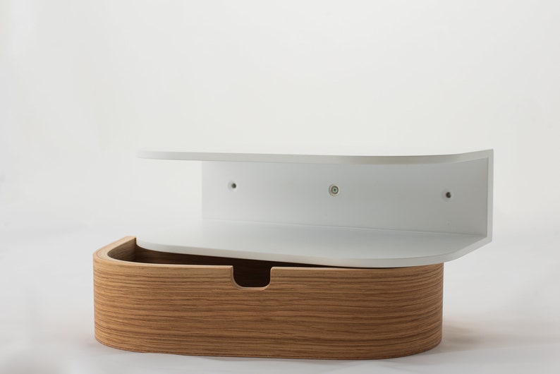 May include: White wall-mounted shelf with a curved front and a wooden drawer underneath. The shelf has three screw holes on the back.