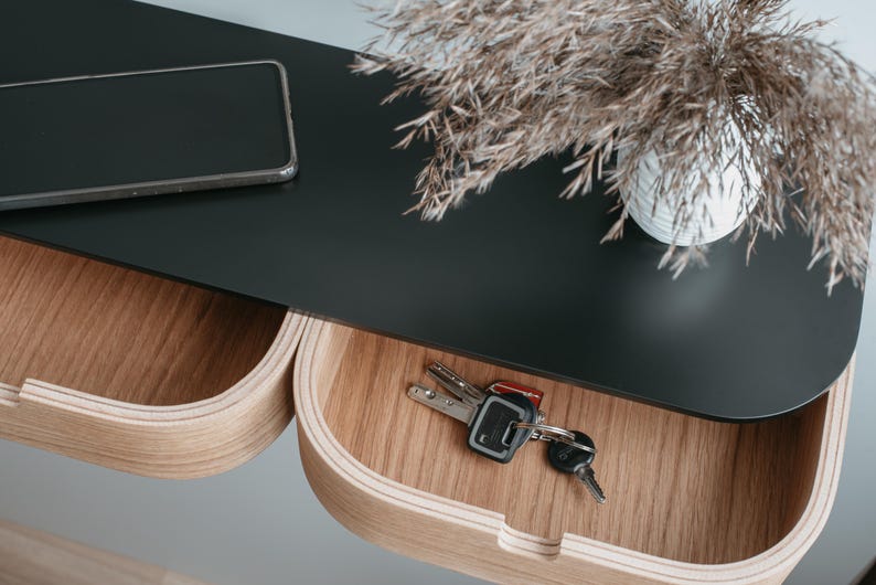 May include: A black shelf with two wooden drawers. The top shelf has a black smartphone and a vase with dried flowers. The bottom drawer has a set of keys.