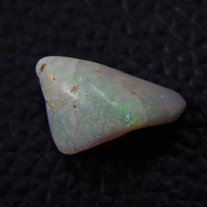 May include: A polished opal gemstone, shaped like a teardrop. The stone has a milky white base with flashes of iridescent green and blue. The opal is smooth and translucent, displaying its natural beauty. A unique piece.